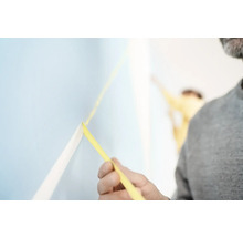 Mann bringt Malerband auf einer Wand an.