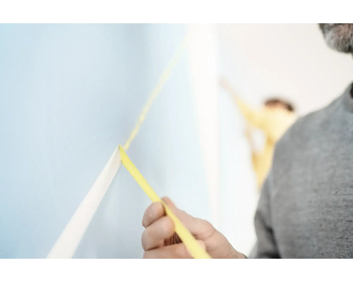 Mann bringt Malerband auf einer Wand an.