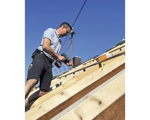 Handwerker befestigt mit einem Akkuschrauber Schrauben auf einem Dachstuhl.