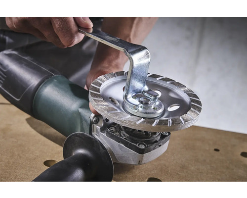 Une personne change un disque à tronçonner sur une meuleuse d''angle avec une clé à fourche.