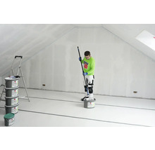 Ein Mann streicht einen Dachboden mit einer Farbrolle, Eimer mit Farbe und eine Leiter sind ebenfalls vorhanden