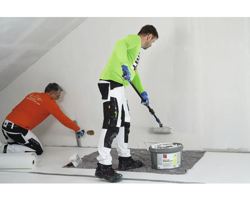 Zwei Handwerker tragen Rollspachtel auf eine Wand auf. Einer verwendet eine Rolle, der andere eine Spachtel.