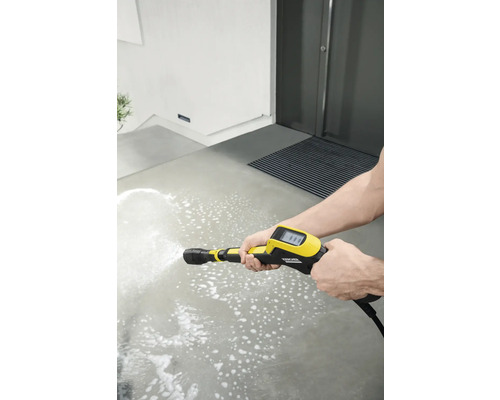 Une personne nettoie une surface en béton avec un nettoyeur haute pression jaune.