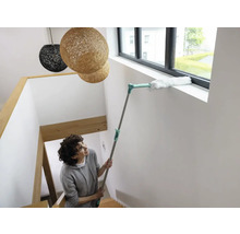 Femme nettoie le cadre de fenêtre avec un plumeau sur une tige télescopique dans la cage d''escalier