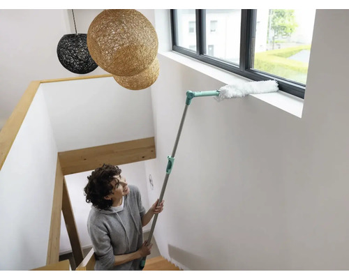Frau reinigt Fensterrahmen mit Staubwedel an Teleskopstiel im Treppenhaus