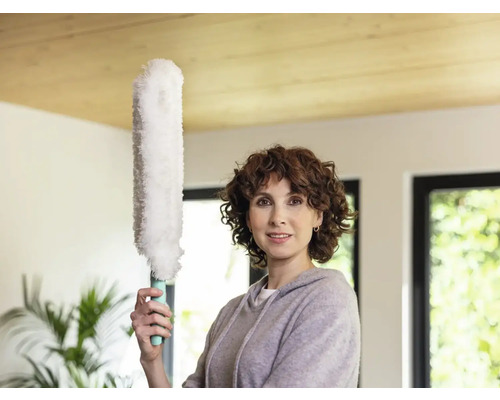 Frau hält Staubwedel in einem hellen Raum.