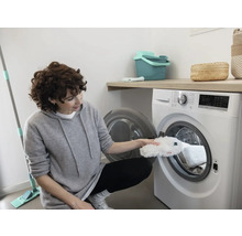Une femme met une housse de balai à franges dans un lave-linge