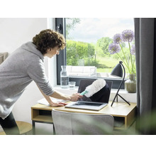 Femme nettoie un ordinateur portable avec un plumeau sur un bureau.