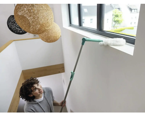 Frau reinigt Fensterrahmen mit einem Staubwedel.