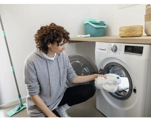 Frau legt Moppbezüge in die Waschmaschine in einem hellen Raum.