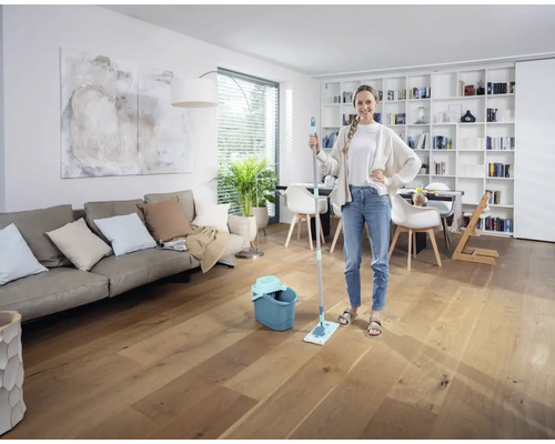 Femme avec une serpillière et un seau dans un salon lumineux sur un plancher en bois