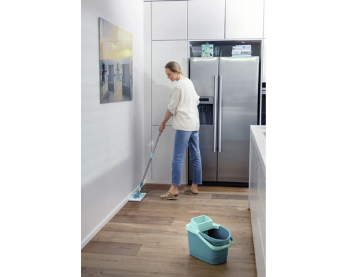 Femme nettoie le sol avec une serpillière dans une cuisine.