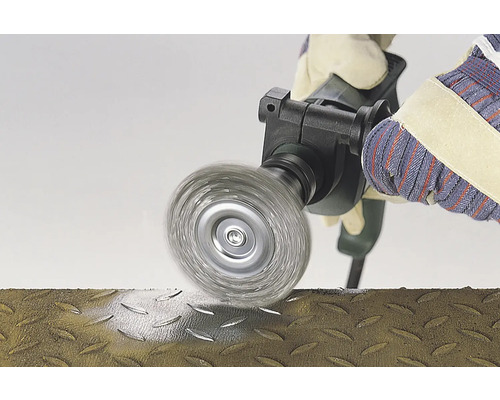 Brosse métallique en utilisation sur une surface métallique, manipulée par une personne portant des gants.