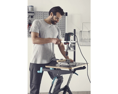 Mann mit Schutzbrille bohrt mit einer Bohrmaschine in ein Werkstück auf einem Werktisch.