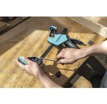 Un artisan fixe une pièce à travailler avec une serre-joint à une main et une clé Allen sur un établi.