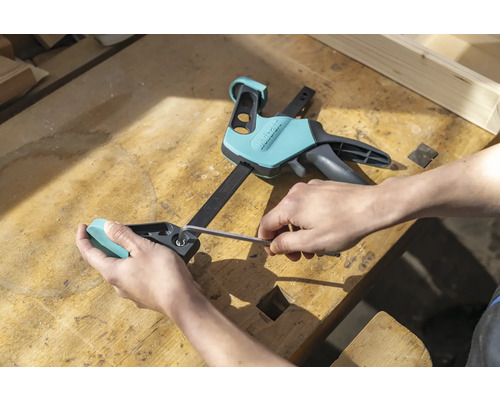 Person justiert eine Einhandzwinge mit einem Inbusschlüssel auf einer Werkbank.