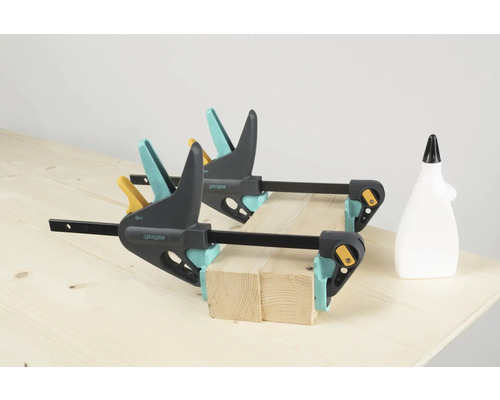 Deux serre-joints à une main Wolfcraft fixent des morceaux de bois sur un établi, un flacon de colle est posé à côté.