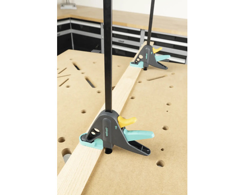 Deux serre-joints à une main Wolfcraft fixent une pièce sur un établi.