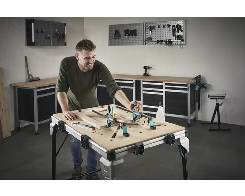 Un homme travaille sur un cadre en bois sur un établi dans un atelier. Des outils et du matériel d''atelier sont visibles en arrière-plan.