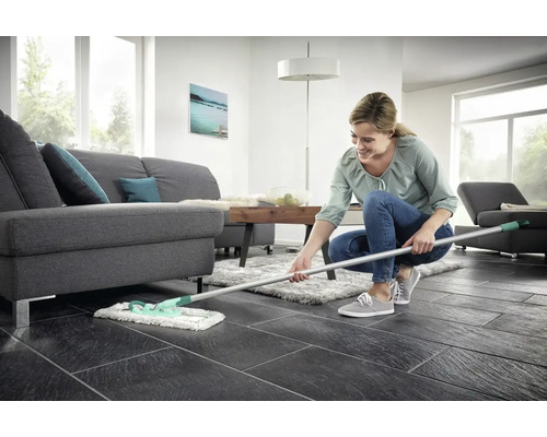 Frau wischt Boden im Wohnzimmer mit Mopp