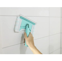 Main utilisant un racloir à vitres avec housse microfibre sur un mur carrelé