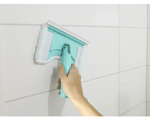 Main utilisant un racloir à vitres avec housse microfibre sur un mur carrelé