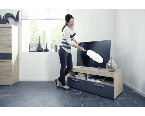 Frau wischt Staub von einem Fernseher mit einem Staubwedel in einem Wohnzimmer.