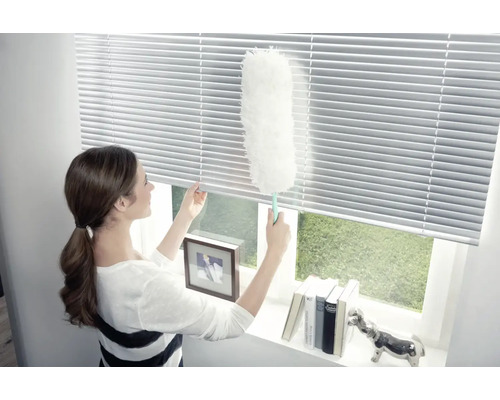 Frau reinigt Jalousien mit einem Staubwedel