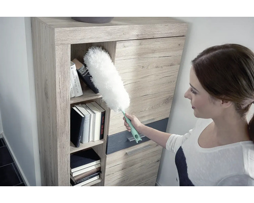 Frau reinigt Regal mit Staubwedel