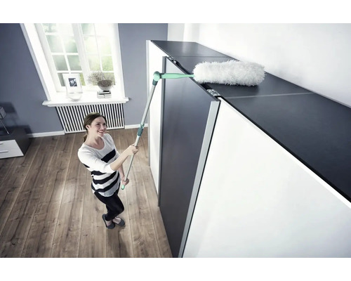 Frau reinigt eine Schrankoberfläche mit einem Staubwischer.