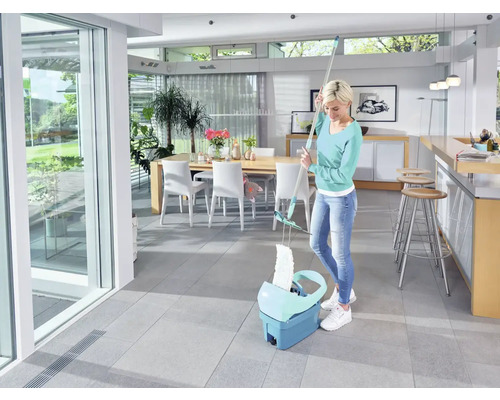 Frau wischt Boden mit einem Mopp und Eimer in einem hellen Raum.