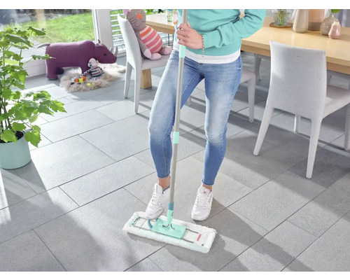 Frau wischt Fliesenboden mit Mopp in einem hellen Raum.