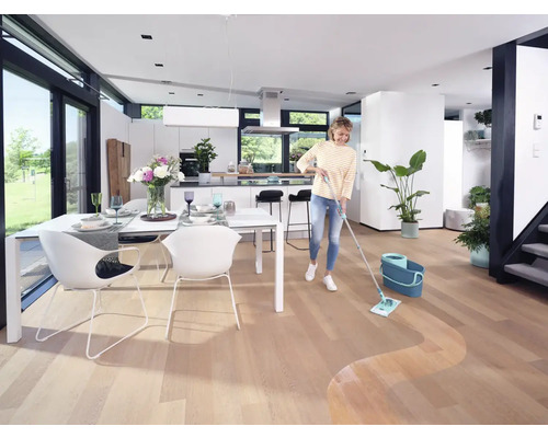 Frau wischt Holzboden in hellem Wohnraum mit Mop und Eimer