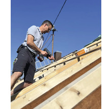 Handwerker befestigt Dachlatten mit einem Akkuschrauber auf einem Dachstuhl.