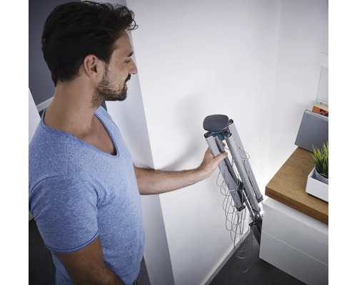 Mann hält einen zusammengeklappten Wäscheständer in einem Raum.