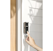 Un doigt appuie sur le bouton d'une sonnette vidéo Imou installée sur un cadre de porte clair à côté d'une porte en bois.