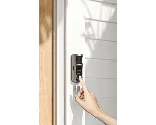 Un doigt appuie sur le bouton d'une sonnette vidéo Imou installée sur un cadre de porte clair à côté d'une porte en bois.