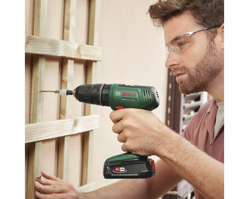 Un homme visse une vis dans une construction en bois avec une visseuse à percussion sans fil Bosch