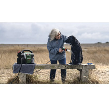 Femme lavant un chien avec un nettoyeur haute pression portable à l'extérieur.