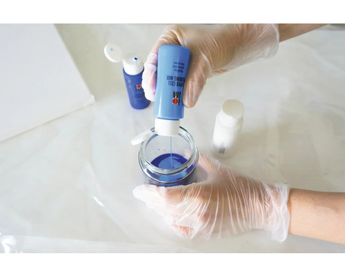 Une personne mélange de la peinture de résine de coulée bleue dans un récipient en verre pour des projets artistiques.