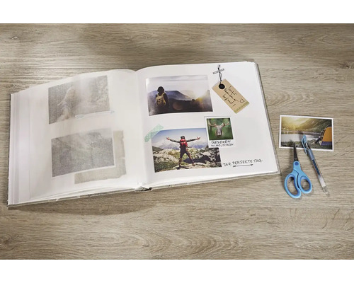 Album photo ouvert avec des photos collées, un stylo et des ciseaux sur une table
