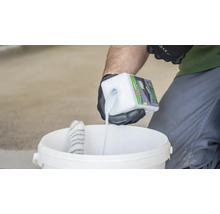 Eine Person giesst Grundierung in einen Eimer zum Auftragen mit einer Farbwalze.