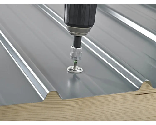 Fixation d'une plaque de tôle trapézoïdale avec un tournevis sur une planche de bois.