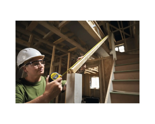 Une femme mesure du bois avec un mètre ruban Stanley sur un chantier.