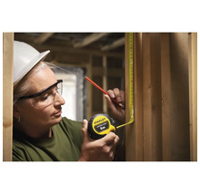 Une femme mesure une planche en bois avec un mètre ruban jaune de Stanley.