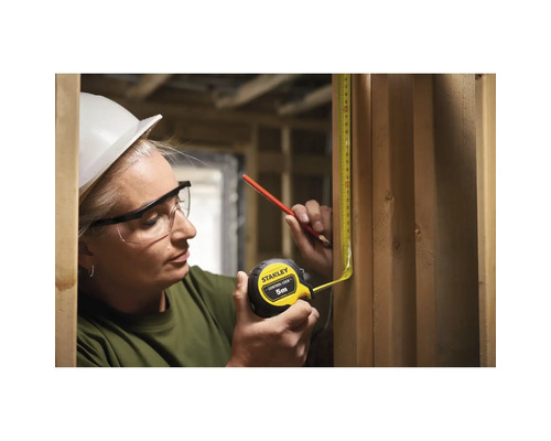 Une femme mesure une planche en bois avec un mètre ruban jaune de Stanley.