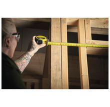 Une personne mesure un cadre en bois avec un mètre ruban Stanley jaune.