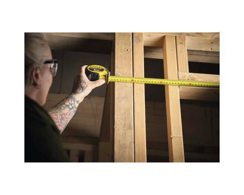Une personne mesure un cadre en bois avec un mètre ruban Stanley jaune.