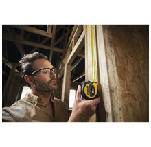 Un homme mesure une planche de bois avec un mètre à ruban Stanley