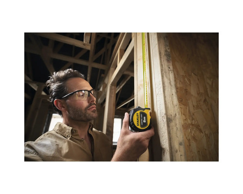 Un homme mesure une planche de bois avec un mètre à ruban Stanley